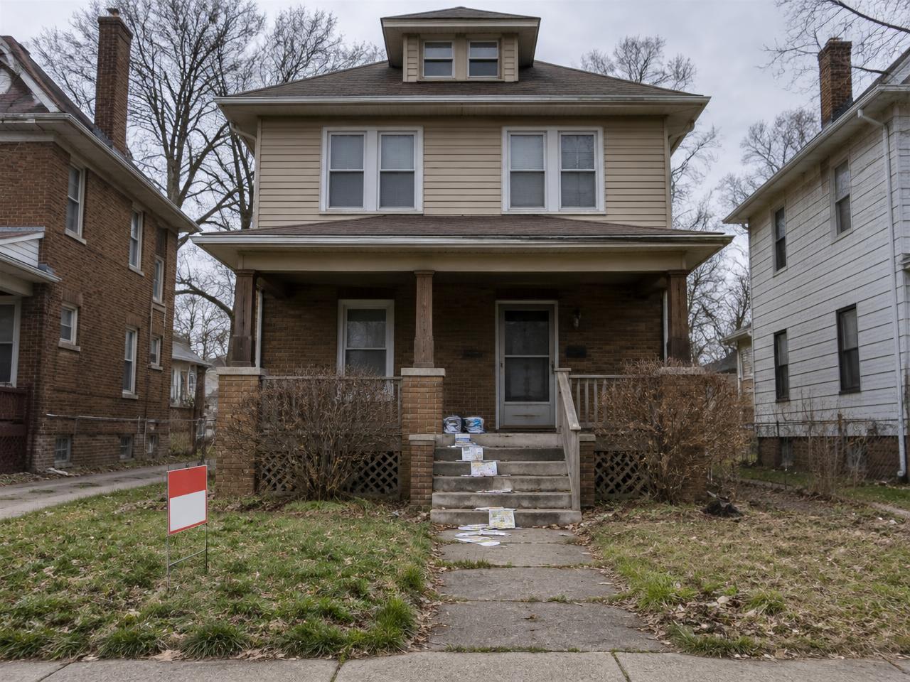 Detroit home with a rental sign in the yard and mail piled up on the porch steps